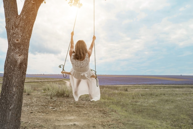 Girl on a swing wrapped in green foliage they are dressed in white robes the sun shines on them