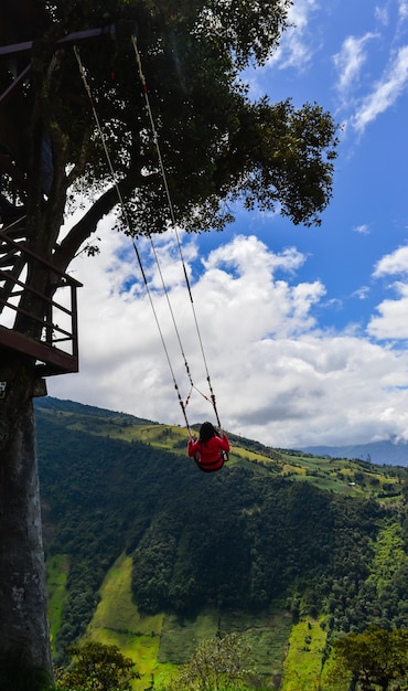 Девушка качается в домике на дереве, расположенном на Банос, Эквадор, на вершине горы Тунгурахуа, за вулканом