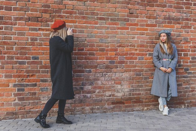 Girl takes picture of her female friend in front of brick wall in city street photographer and vintage camera hobby concept