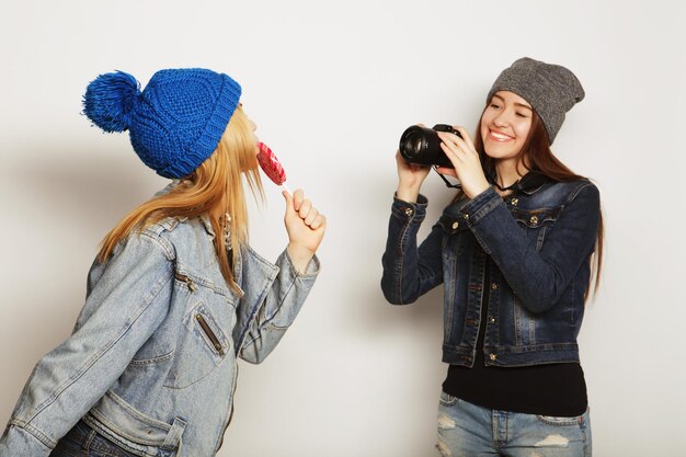 A girl takes picture of her friend in front over white backgrounf