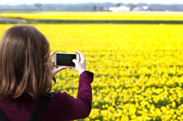 女の子がスマートフォンで黄色い水仙の写真を撮る