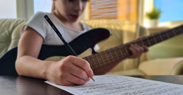 Девушка делает заметки в учебнике, играет на гитаре дома.