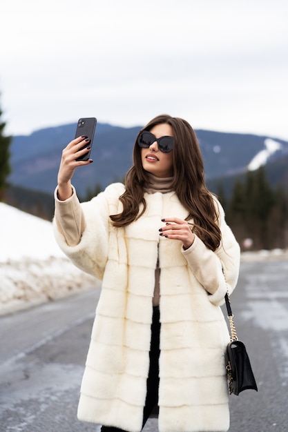 冬の山の上のスマートフォンで彼女の自己の写真を取っている女の子