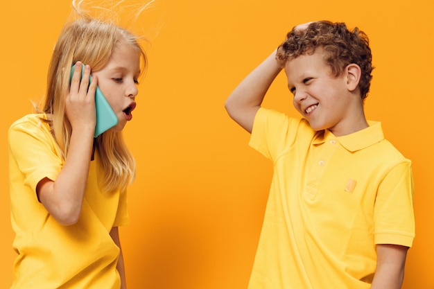 Girl talking on phone standing by brother against yellow background