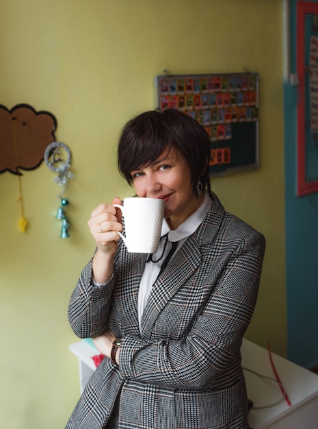 A girl teacher stands in the classroom and drinks tea