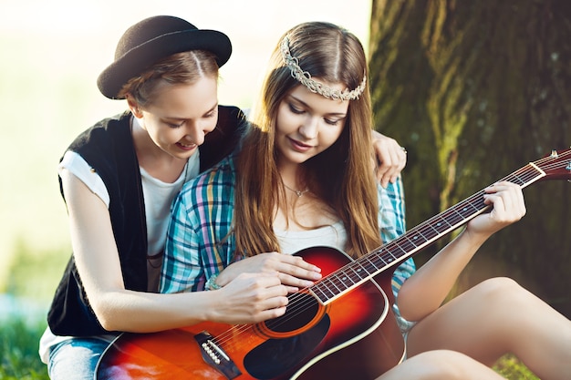 Girl teaching her friend to play guitar in the park