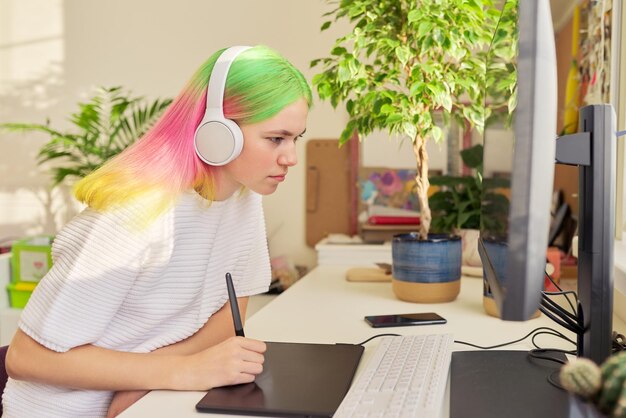 Girl teenager artist in headphones drawing on computer using graphics tablet