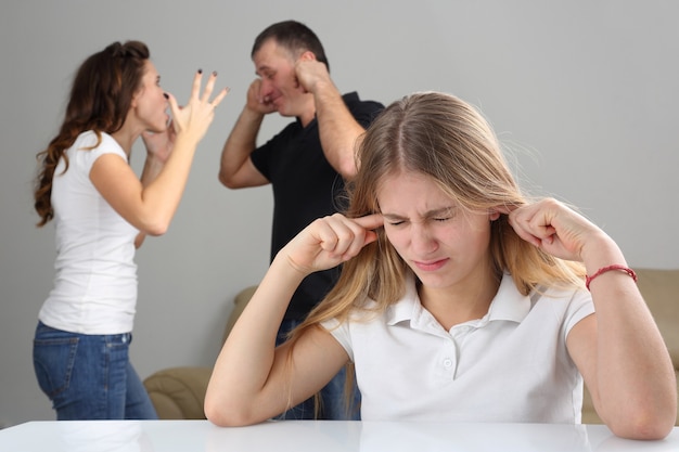 Girl teenager closes ears in the background screaming at each other parents