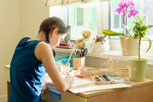 Girl teenager draws watercolor, sitting at home at the table