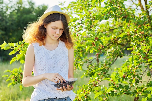 Girl teenager eating delicious healthy mulberries from the tree, summer garden harvest of ripe berries, season of vitamin organic natural berries and fruits