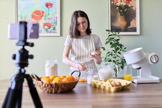 여자 십대 음식 블로거는 부엌에서 오렌지 팬케이크를 요리합니다. 여자는 설탕 가루, 현대 청소년, 취미 및 여가, 건강에 좋은 맛있는 홈메이드 음식 개념을 붓는다
