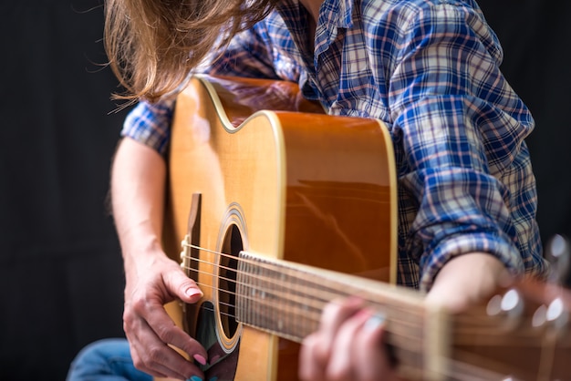 Girl teenager playing an acoustic guitar on a dark background in the Studio. Concert young musicians