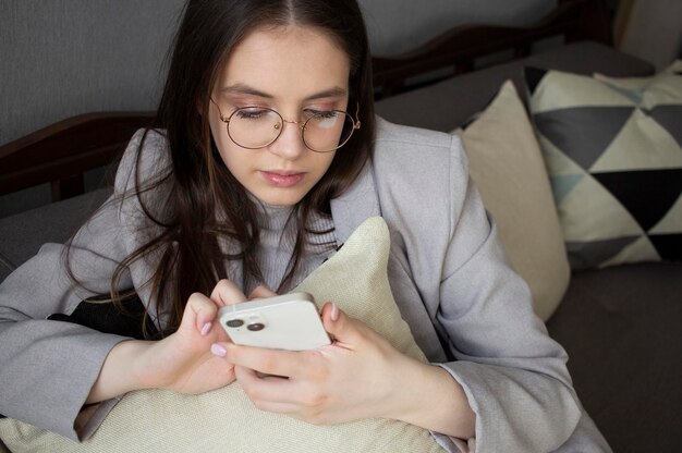 Girl teenager sitting on the couch with pillows looks at the smartphone