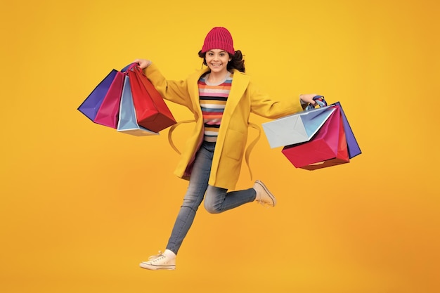 Girl teenager with shopping bags isolated on yellow backgound winter shopping sale run and jump