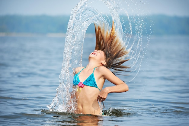 Girl teenager with splashes from hair on lake