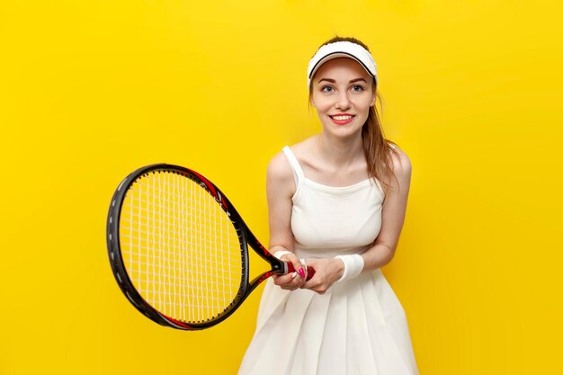 Girl tennis player in sportswear holding tennis racket on yellow background and smiling