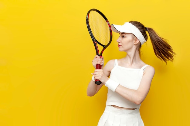 girl tennis player in sportswear holding tennis racket on yellow isolated background and smiling