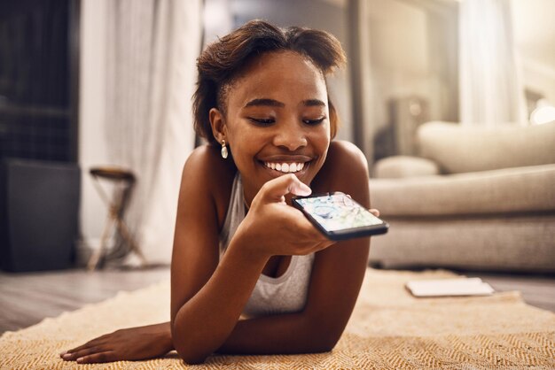 Girl texting chatting and browsing social media on her phone while relaxing at home Young woman searching an online app enjoying free time and having fun with an app on her living room floor