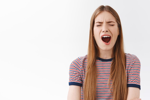 Girl too tired of boring talks yawning Sleepy cute unamused european woman in striped tshirt open mouth and close eyes from fatigue stand white background uninterested white background