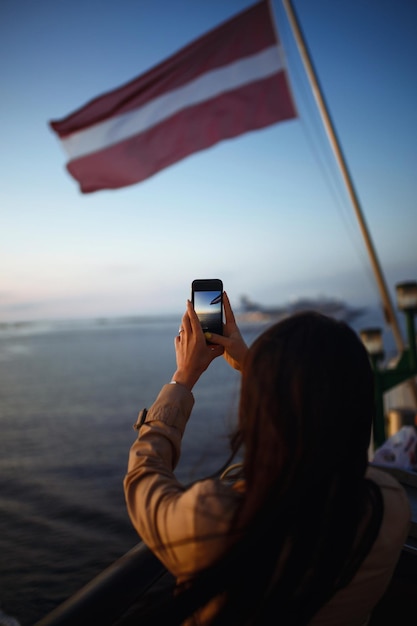 Девушка-туристка фотографирует лайнер на закате на озере в Норвегии Туристка фотографирует закат на телефон