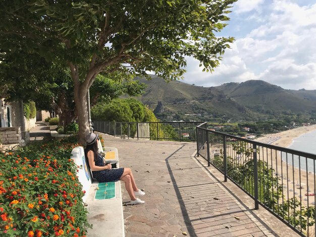 女の子の観光客はベンチに座って、イタリアの海を見ます