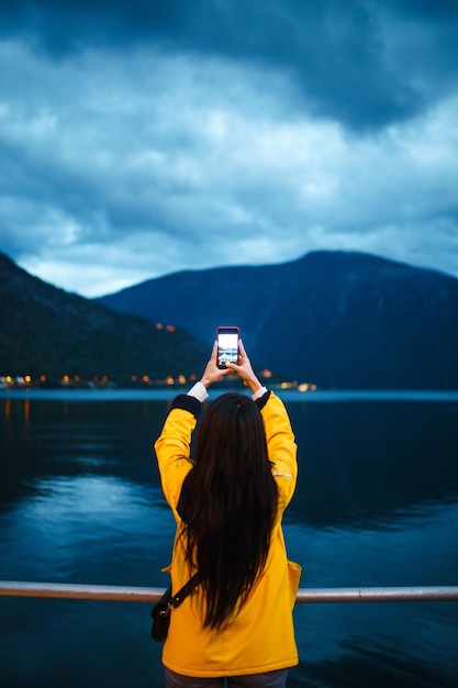 女の子の観光客は、ノルウェーの湖のほとりで電話で写真を撮ります アクティブな女性がリラックス