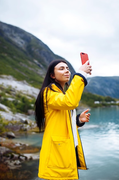 女の子の観光客は、ノルウェーの湖のほとりで電話で写真を撮ります アクティブな女性がリラックス