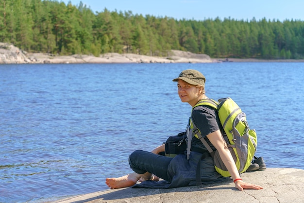 Girl tourist with a backpack sits on the shore of the lake