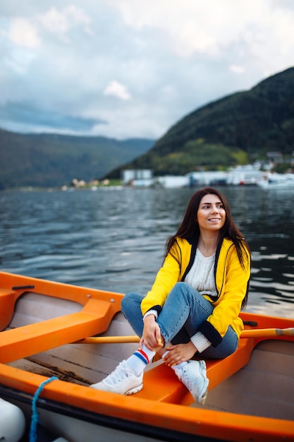 Girl tourist in yellow jacket is sitting and posing in a boat against the backdrop of the mountains