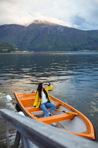 Girl tourist in yellow jacket is sitting and posing in a boat against the backdrop of the mountains