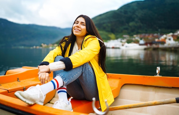 노란색 재킷을 입은 소녀 관광객이 노르웨이 여행 라이프스타일 모험에서 보트에 포즈를 취하고 있습니다.