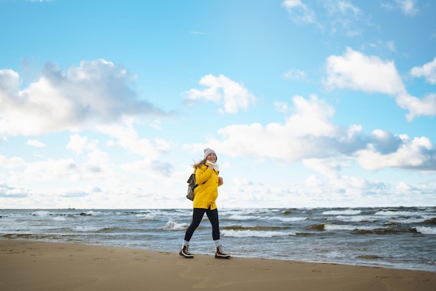 黄色いジャケットを着た少女が海辺でポーズをとり旅のライフスタイルを冒険しています