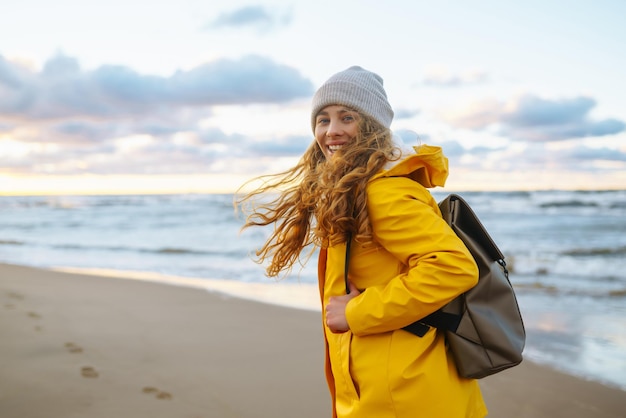 黄色いジャケットを着た少女が海辺でポーズをとり旅のライフスタイルを冒険しています