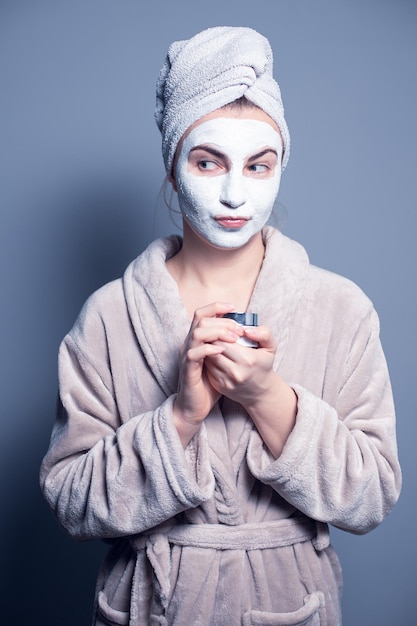 Girl in a towel on her head in a cosmetic mask on a gray background