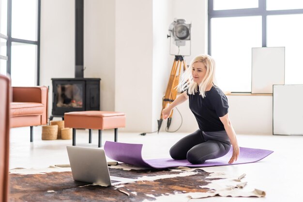 Girl training at home and watching videos on laptop, training in living room.