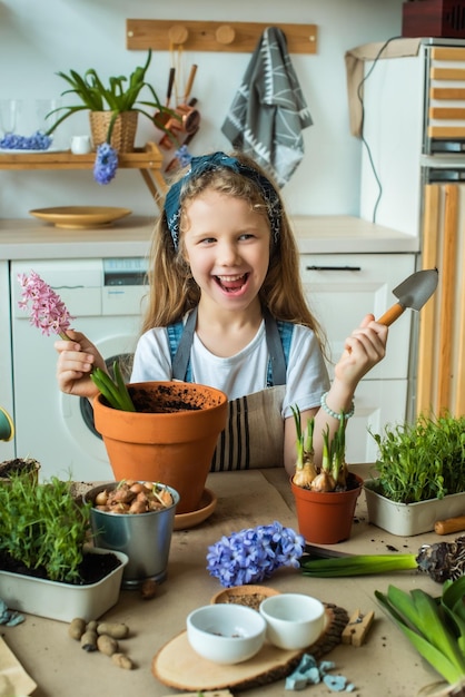 Girl transplants flowers and houseplants a child in a bandana plants bulbs hyacinths microgreens
