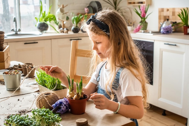 Girl transplants flowers and houseplants a child in a bandana plants bulbs hyacinths microgreens