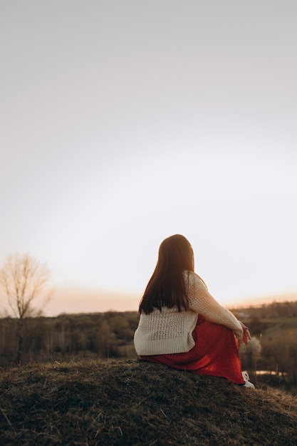 여자 여행자는 산꼭대기에 올라앉아 일몰과 안개를 바라보고 있다