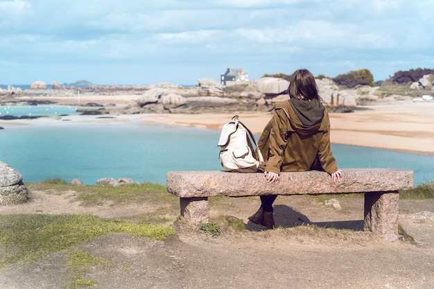 女の子の旅行者は、ブルターニュのトレガステルの海と海岸近くのベンチに座っています。フランス