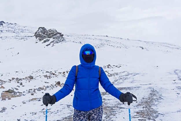 Girl traveler or skier in warm clothes, windproof mask and windproof glasses in the winter mountains