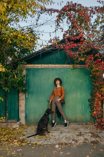 Photo girl in trendy vintage clothes stands in the autumn day outdoors on the background of a green garage