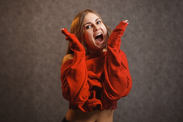 Girl tries on a red sweater on a gray background