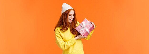 Girl trying figureout whats inside gift box shaking it and looking intrigued excited happy redhead w