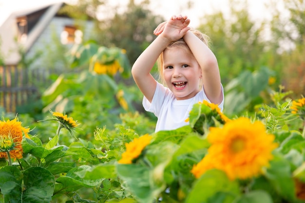 Ragazza in maglietta ha incrociato le braccia sulla testa si trova nel campo di girasoli e sorrisi