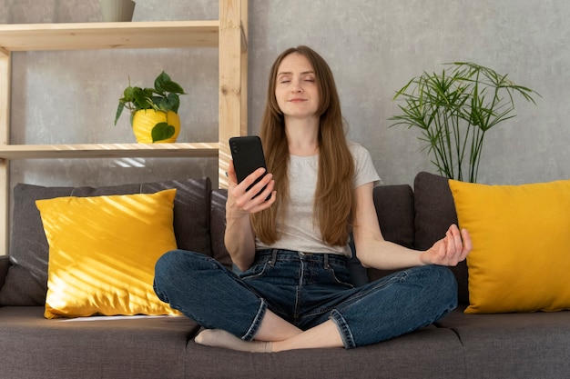 女の子は電話と瞑想でマントラをオンにしました。女性は蓮華座に座り、スマートフォンで瞑想をオンにします。