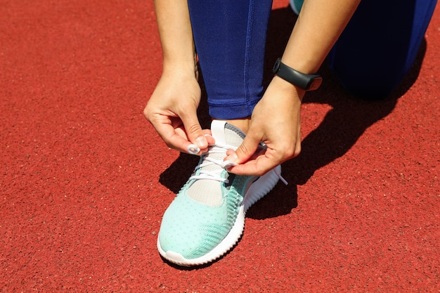 Girl tying shoelaces on red athletic running track, space for text