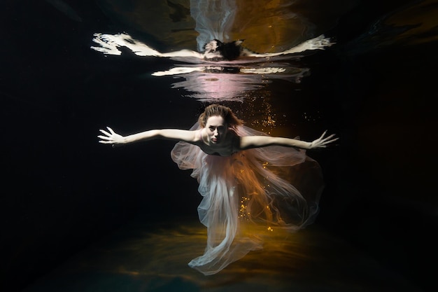 A girl underwater in the pool of a photo studio in a dress