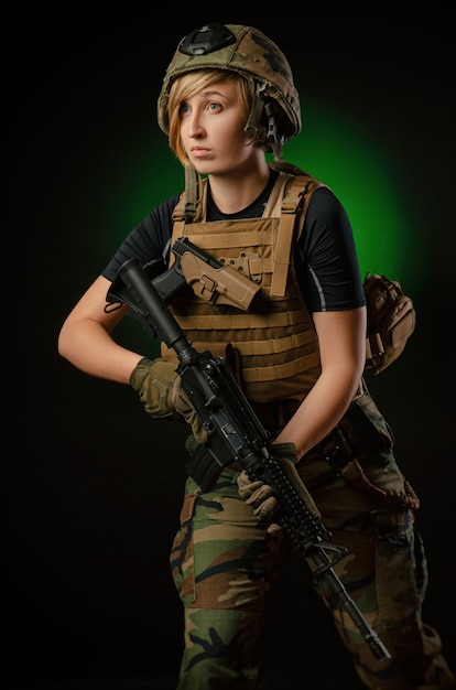 The girl in uniform with a gun posing, aiming, reloading, shooting, on a dark background in the Studio