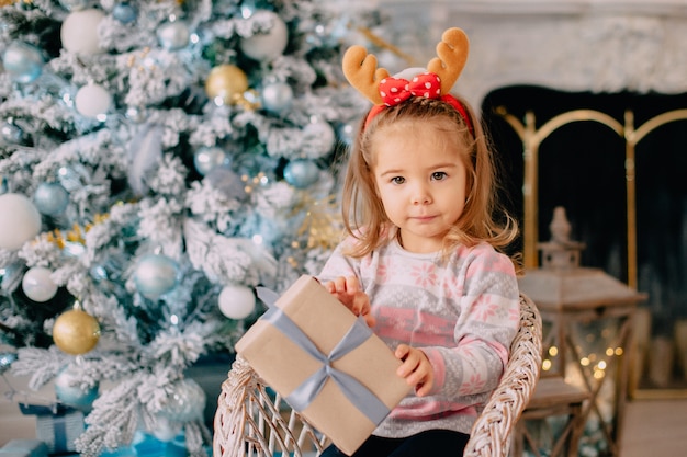 Girl unpacks gift on background of Christmas tree