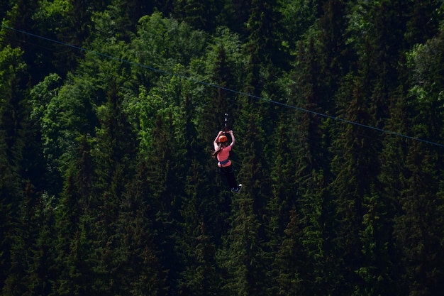 A girl of unrecognizable appearance descends a tightrope on a zipline at high altitude